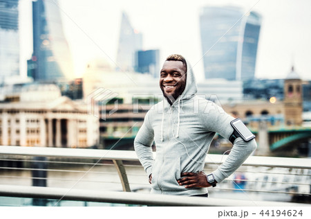 Black man runner with smart watch and smartphone on the bridge in a city, resting. 44194624