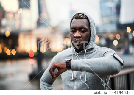 Black man runner with smartphone in an armband on the bridge in London, resting. 44194632