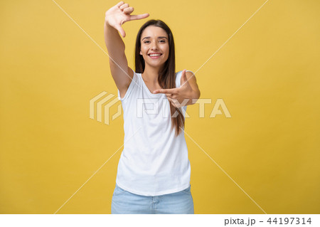 Young beautiful woman over isolated yellow background smiling making frame with hands and fingers Young beautiful woman over isolated yellow background smiling making frame with hands and fingers 44197314