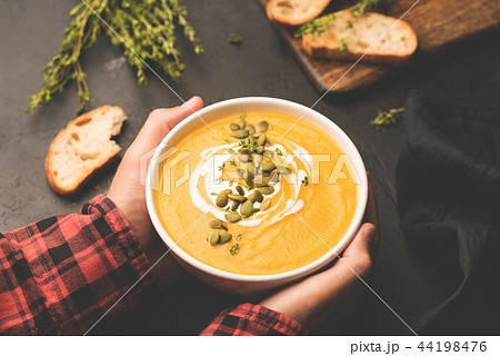Person holding bowl of warm pumpkin soup in hands 44198476