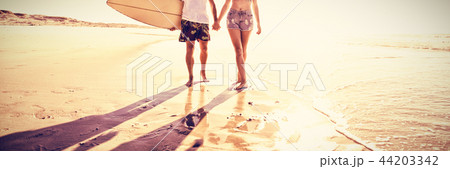 Young couple holding hands at beach during sunny day Young couple holding hands at beach during sunny day 44203342