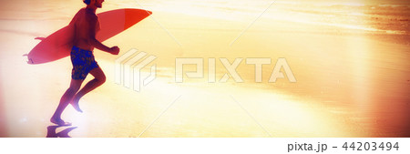 Shirtless man running while holding surfboard at beach Shirtless man running while holding surfboard at beach 44203494