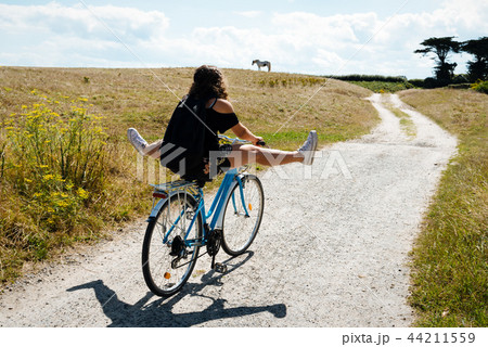 Pretty young woman riding bicycle in a country road  44211559