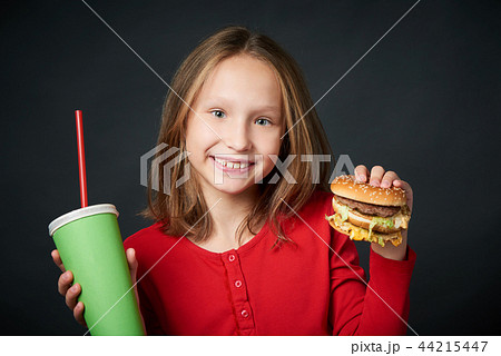 Closeup of smiling girl holding hamburger and paper cup Closeup of smiling girl holding hamburger and paper cup 44215447