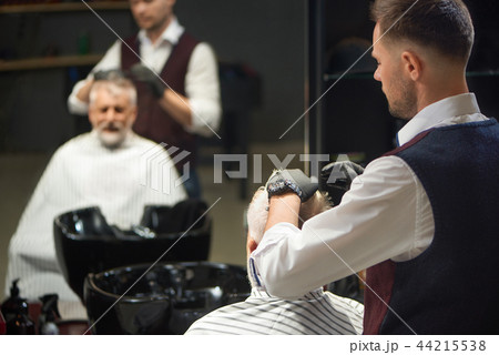 Barber in black gloves grooming and styling haircut of client. 44215538