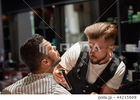 Concentrated male hairdresser holding trimmer in hands. Concentrated male hairdresser holding trimmer in hands. 44215609