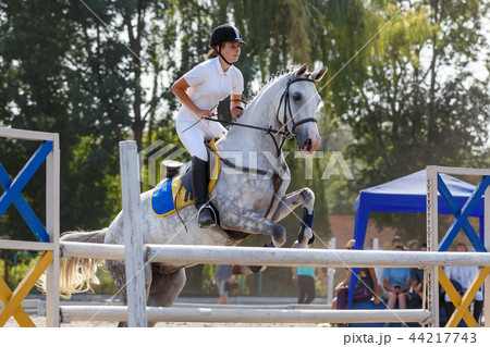 Equestrian sport. Young girl jumping over obstacle 44217743