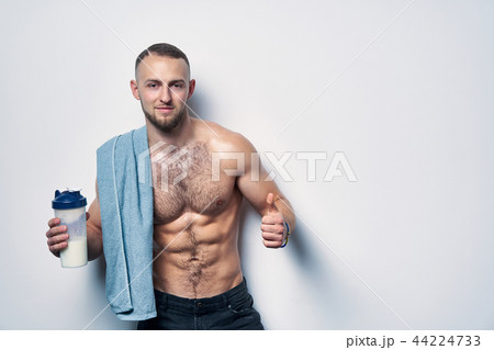Muscular man shirtless with towel over shoulders holding rotein drink in shaker 44224733