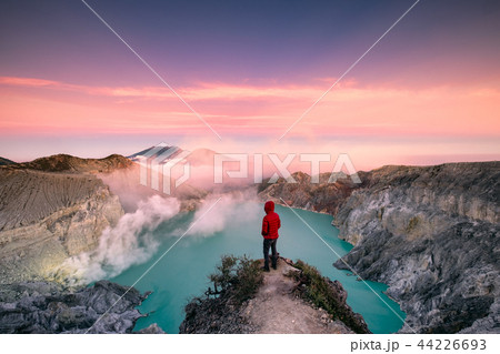 Man standing on edge of crater with colorful sky 44226693