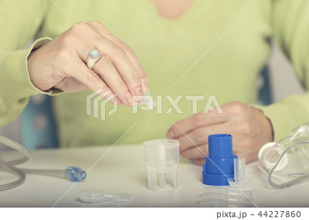 Female hand puts drug in a nebuliser container.  44227860