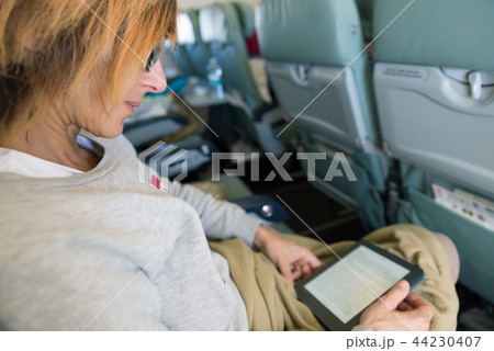 Woman reading ebook sitting inside airplane 44230407