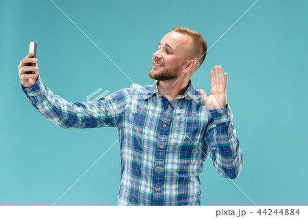 Portrait of attractive young man taking a selfie with his smartphone. Isolated on blue background. Portrait of attractive young man taking a selfie with his smartphone. Isolated on blue background. 44244884