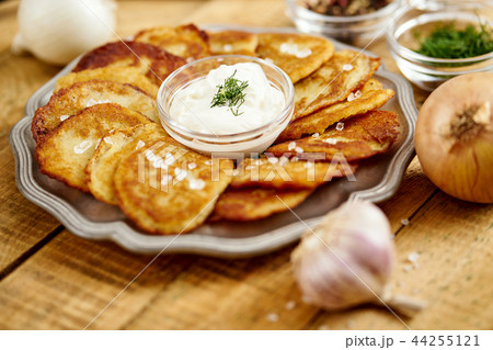 metal plate with delicious potato pancakes on an old wooden table with garlic onions and toppings metal plate with delicious potato pancakes on an old wooden table with garlic onions and toppings 44255121