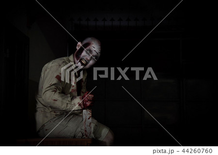 Male zombie sitting and smiles in dark room Male zombie sitting and smiles in dark room 44260760
