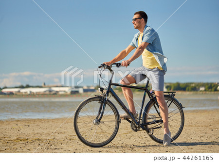 happy man riding bicycle along summer beach 44261165
