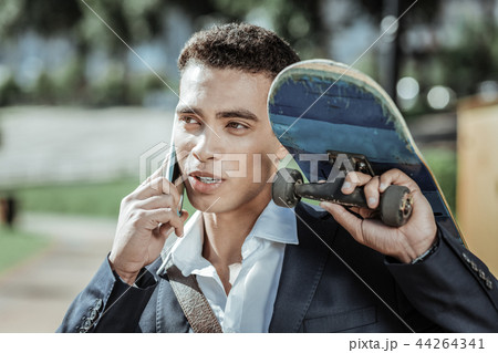 Charming male student calling friends with skateboard Charming male student calling friends with skateboard 44264341