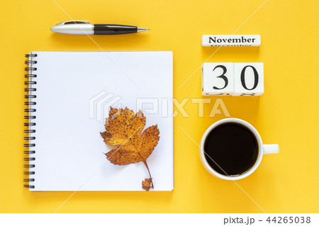 calendar November 30 cup of coffee, notepad with pen and yellow leaf on yellow background 44265038