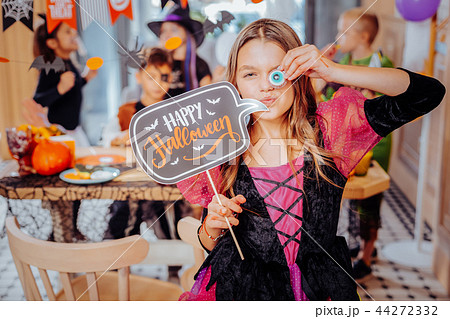 Funny cute schoolgirl holding funny cookies while attending Halloween party Funny cute schoolgirl holding funny cookies while attending Halloween party 44272332