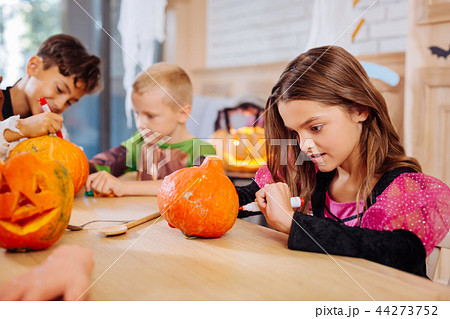 Beautiful dark-haired girl wearing pink and black Halloween dress coloring pumpkin 44273752