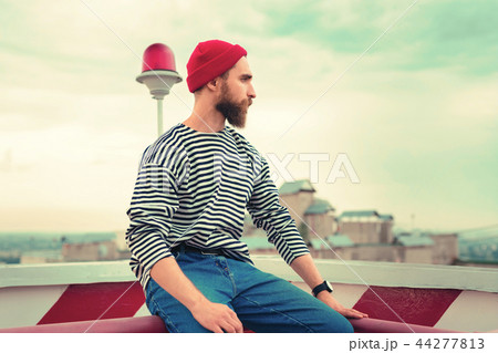 Calm man in red hat sitting on the roof and looking into the distance 44277813