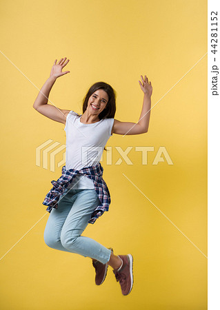 Full-length portrait of carefree girl in white shirt and jean jumping on yellow background. 44281152
