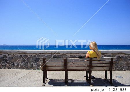 Young woman yellow t-shirt resting on the seafront on a wooden bench Young woman yellow t-shirt resting on the seafront on a wooden bench 44284983