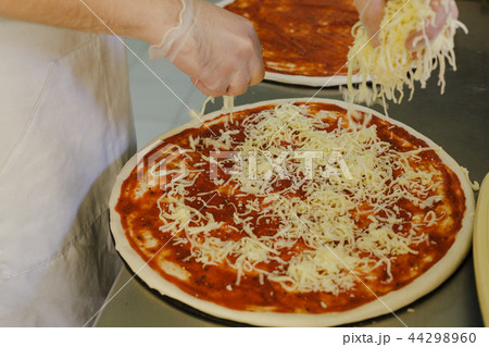 Cheese being spread on tomato sauce on pizza base 44298960