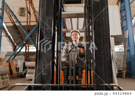 man driving a forklift through a warehouse in a factory. driver in uniform and protective helmet 44314664