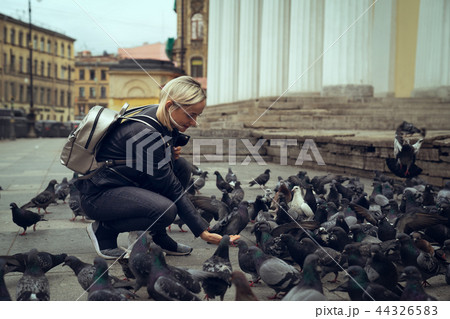 Young beautiful woman is feeding pigeons with bread crumbs in the town square on autumn day 44326583