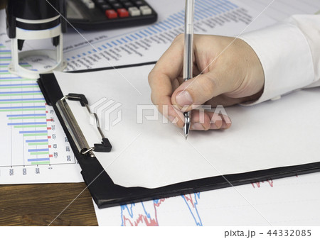 A man's hand holds a pen on a blank sheet, calculator, a seal A man's hand holds a pen on a blank sheet, calculator, a seal 44332085
