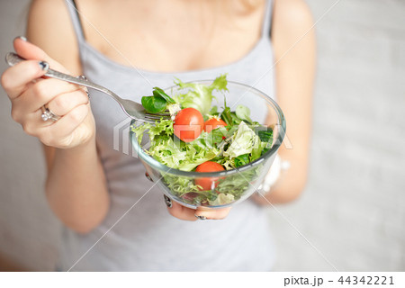 Close-up rear view woman holding bowl of fresh vegetable salad holding fork in hand Close-up rear view woman holding bowl of fresh vegetable salad holding fork in hand 44342221