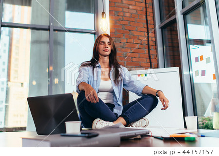 Female student sitting in lotus pose on table in her room meditating relaxing after studying and 44352157