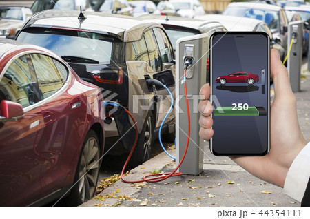 Hand with phone. Electric car charging point. Hand with phone. Electric car charging point. 44354111