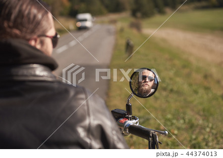 Smiling face of handsome bearded happy biker in dark sunglasses reflected in motorbike mirror. Smiling face of handsome bearded happy biker in dark sunglasses reflected in motorbike mirror. 44374013