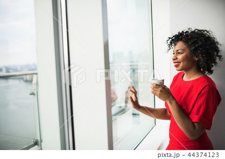 A woman standing by the window holding coffee cup, looking out. Copy space. 44374123