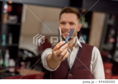 Male hairdresser looking at camera and holding instrument for hair. 44406000