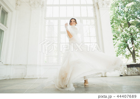 Beautiful bride in wedding dress with long full skirt, white background, dance and smile 44407689
