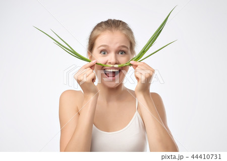 Portrait of beautiful blond woman in a white shirt holding a green onion like a mustache near mouth Portrait of beautiful blond woman in a white shirt holding a green onion like a mustache near mouth 44410731