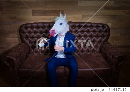 Funny unicorn in elegant suit sits on sofa with bottle of wine Funny unicorn in elegant suit sits on sofa with bottle of wine 44417112