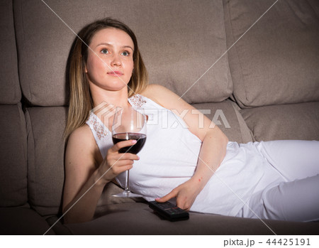 Young woman is sitting with white wine and watching TV Young woman is sitting with white wine and watching TV 44425191