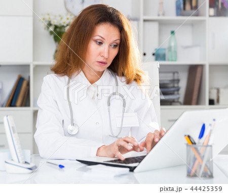 Young therapist woman in uniform is working behind laptop with documents Young therapist woman in uniform is working behind laptop with documents 44425359