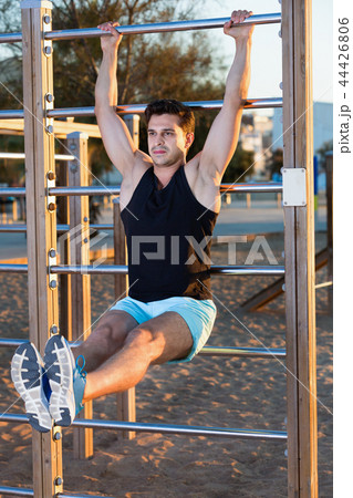 Man doing workout on beach holding L-sit on wall bars 44426806