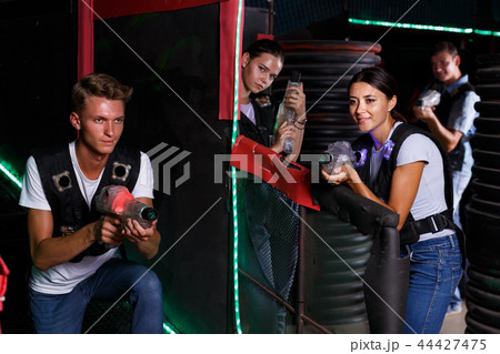 Young men and women in waistcoats playing laser tag game with laser guns Young men and women in waistcoats playing laser tag game with laser guns 44427475