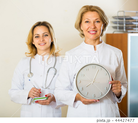 Two female doctors holding clock Two female doctors holding clock 44427477