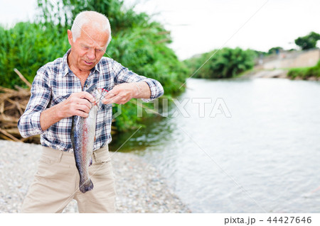 Adult fisherman removing catch from hook Adult fisherman removing catch from hook 44427646