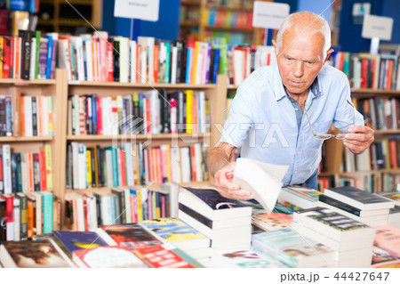 Portrait of intelligent older man choosing necessary books on shelves in library 44427647