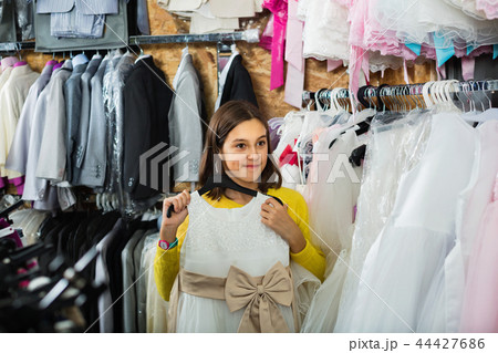 Teenage customer examining dresses in children’s cloths shop Teenage customer examining dresses in children’s cloths shop 44427686