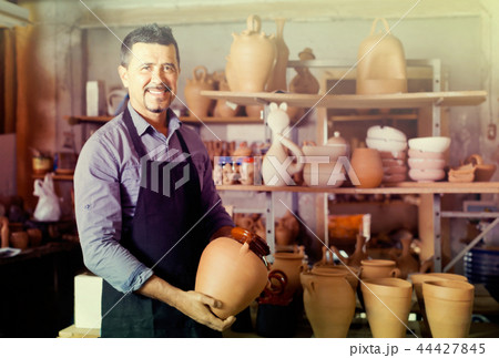 mature man potter holding ceramic vessels 44427845