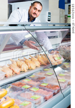 Male shop assistant selling kosher chicken at counter and smiling 44429185