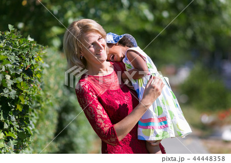 A white woman carries a black girl her shoulder. 44448358